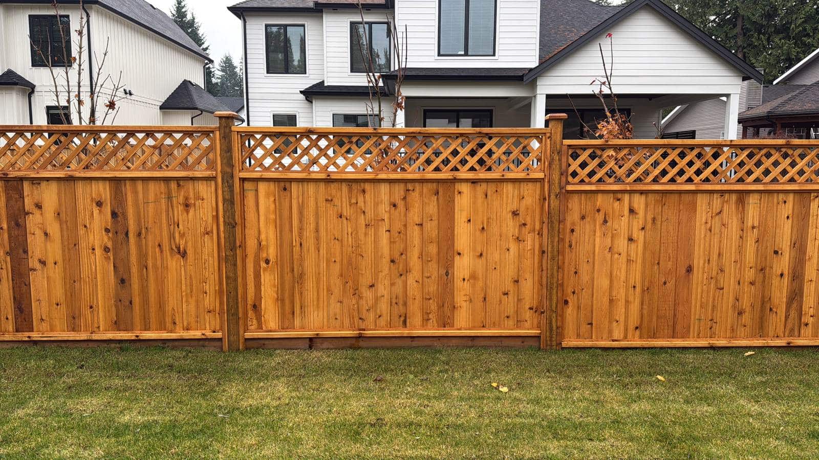 A straight run of cedar fence panels with diagonal lattice tops along a backyard lawn