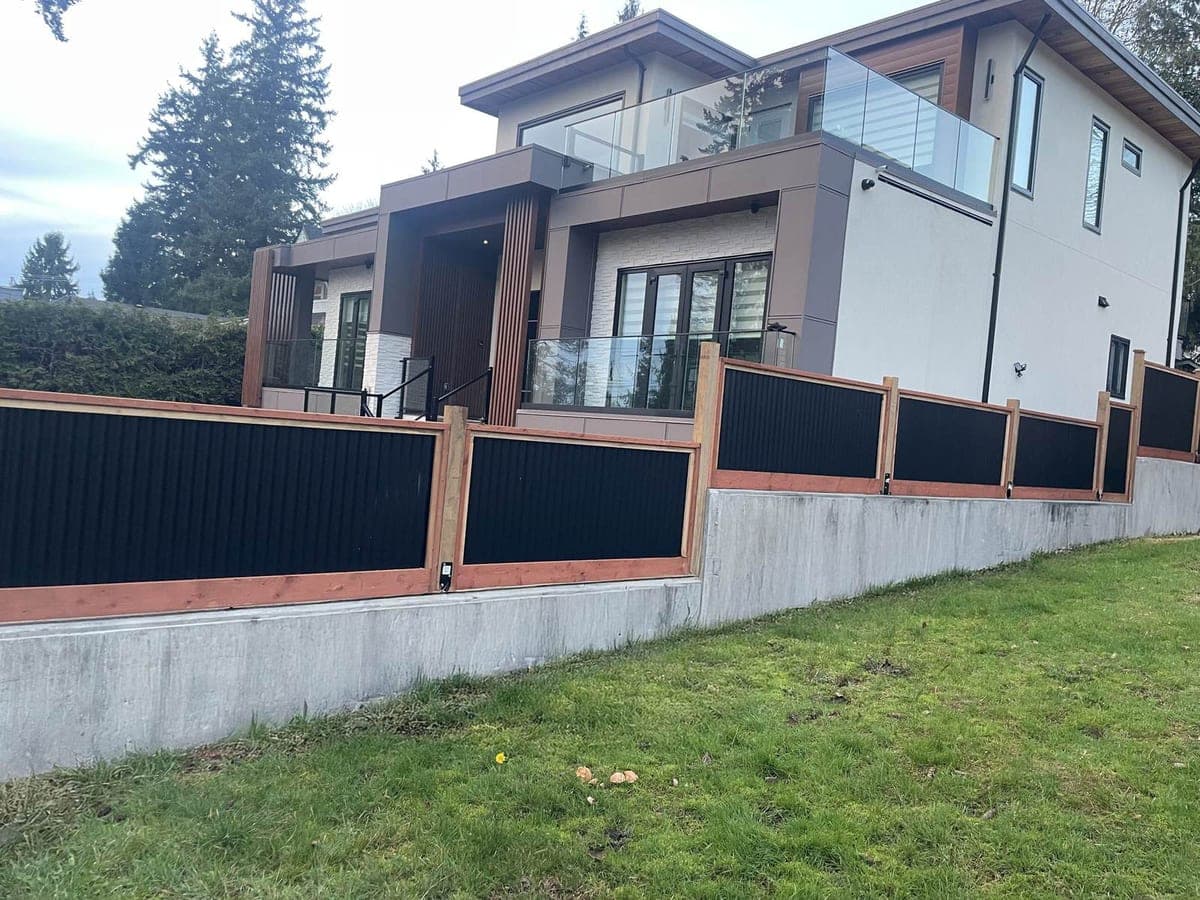 Black corrugated steel fence panels in cedar frames on a concrete retaining wall