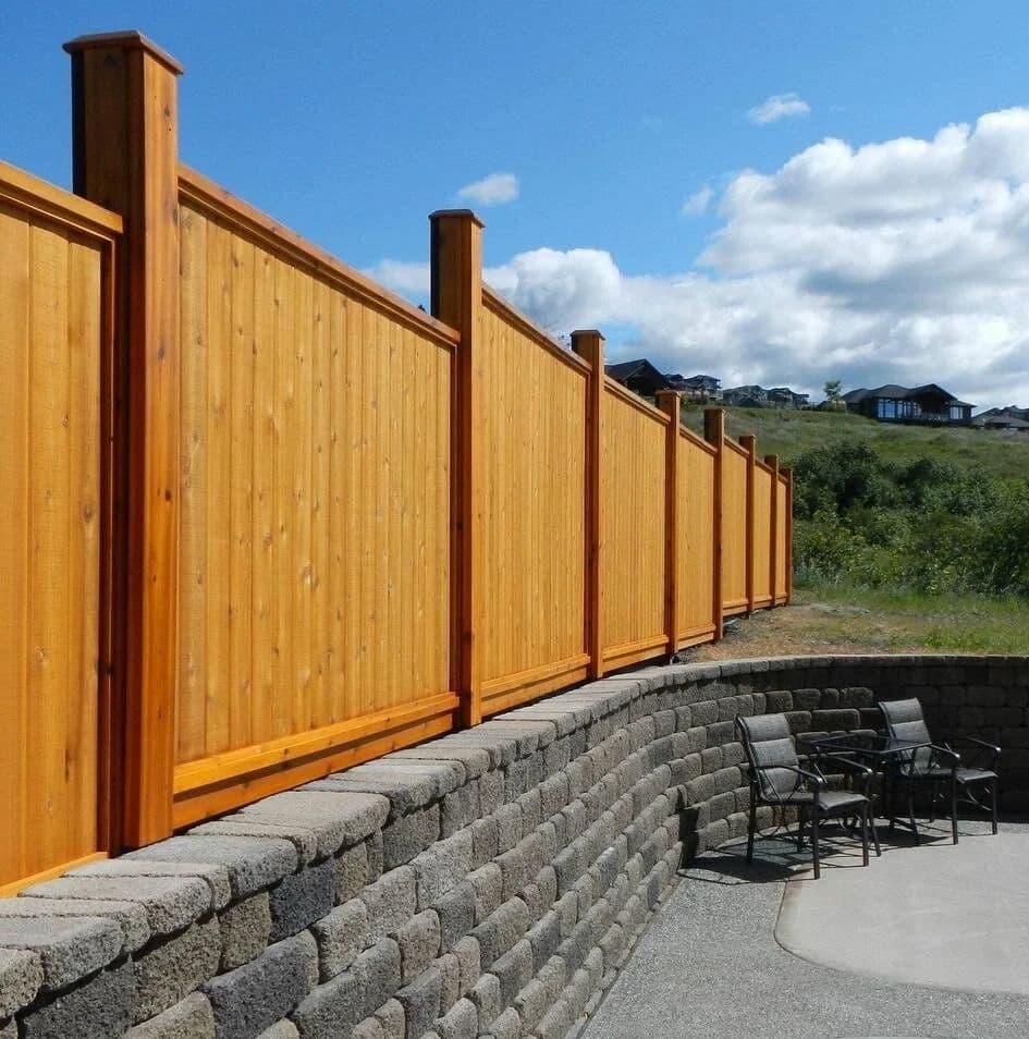 Solid cedar privacy fence stepping along a stone retaining wall beside a patio